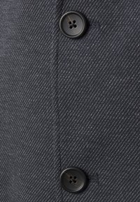 Mörkblått tyg med ett diagonalt mönster och två svarta knappar. Synlig sömnad längs sömmen. Strukturerad yta.