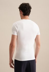 T-shirt blanc ajusté à manches courtes, fabriqué en coton léger et doux. Conception à col rond avec un dos uni et sans embellissement.