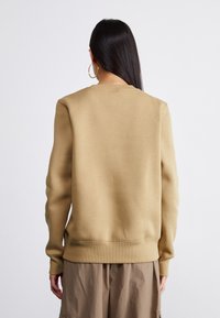 Sweatshirt bege com decote redondo, punhos e barra canelados. Tecido texturizado e corte relaxado. Combinado com calças cargo castanhas claras.