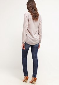 Blusa a maniche lunghe color beige chiaro con piccoli pois bianchi, abbinata a jeans skinny blu scuro e scarpe con tacco marroni.