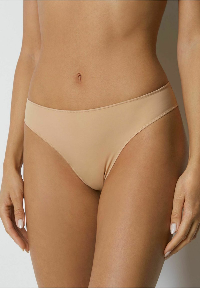 Beige bikiniunderdel med en slät yta, låg skärning och minimala sömmar, designad för komfort och diskret användning under kläder.