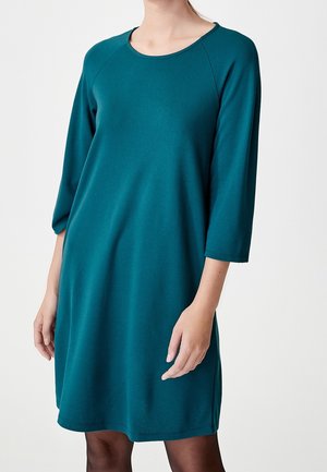 Turkusowa sukienka do kolan wykonana z miękkiego materiału, z okrągłym dekoltem i rękawami o długości trzech czwartek. Prosty fason bez widocznych wzorów czy dodatków.