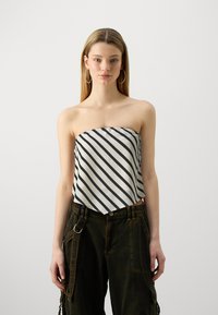 Haut sans bretelles en tissu blanc avec des rayures diagonales bleu marine, présentant un ourlet arrondi. Associé à un pantalon cargo vert foncé et des boucles d'oreilles créoles.
