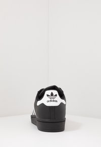 Černý teniska s bílými pruhy, gumovou podrážkou a polstrovaným límcem. Na patě výrazné logo a texturovaný svršek pro lepší úchop.