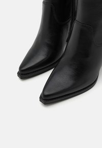 Botines de cuero negro hasta el tobillo con puntera afilada, textura suave, costuras mínimas y cremallera lateral para el cierre.
