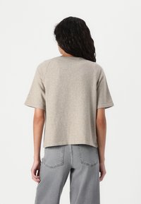 Beige, kortermet strikket topp med avslappet passform. Ribbet halslinning, myk tekstur og en litt avkortet nederste del. Kombinert med høytlivede gråjeans.