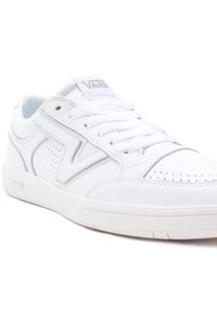 Baskets basses en cuir blanc de Vans avec embout perforé, panneaux latéraux cousus et lacets blancs, présentées légèrement en angle sur fond blanc.