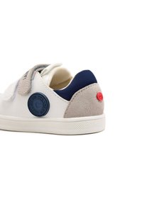 Sneaker bianco con accenti in suede grigio e blu navy. Presenta un logo circolare blu navy e un'etichetta rossa sul tallone. Cinturino in velcro; suola testurizzata.