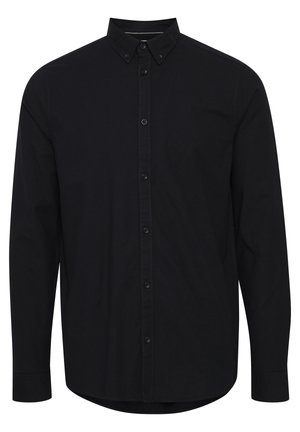 Chemise noire à manches longues en coton. Elle présente un col pointu, une patte de boutonnage à l'avant et un ourlet légèrement arrondi.