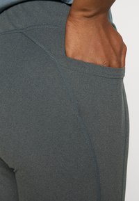 Leggings gris extensibles avec une poche latérale, des coutures plates et une texture lisse, idéales pour le confort et la mobilité.