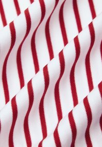 Biała tkanina w czerwone pionowe paski, o gładkiej teksturze i jednolitym wzorze. Paski są równomiernie rozmieszczone i wyraźnie zdefiniowane.