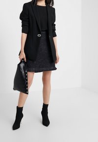 Blazer negro con un toque plateado, combinado con una falda negra texturizada con un dobladillo con flecos y un bolso negro brillante. Botines negros.