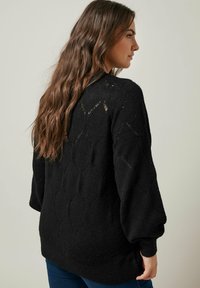Maglione nera lavorata a maglia con un motivo a diamante testurizzato, maniche a palloncino e polsini a coste. Ha una vestibilità rilassata e spacchi laterali.