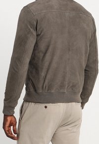 Giacca da uomo in suede grigia con vita a coste, cuciture dettagliate e texture liscia, vista da dietro, caratterizzata da un design pulito.