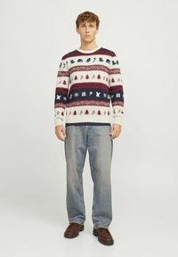 Pull en tricot crème, bleu marine et bordeaux avec des motifs de vacances à motifs. Manches et ourlet côtelés, associé à un jean bleu clair et des chaussures brunes.