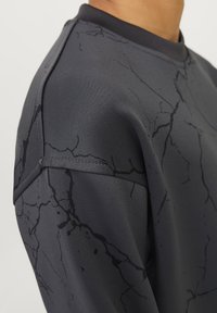 Zbliżenie na ciemnoszary sweatshirt z czarnymi marmurkowymi wzorami i widocznym szwem na ramieniu.