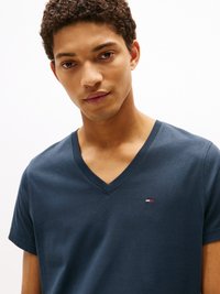 T-shirt azul-marinho com decote em V, feita de tecido macio, com mangas curtas e um pequeno logótipo em vermelho, branco e azul no peito.