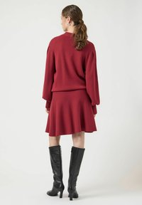 Czerwony sweter robiony na drutach i połączenie spódnicy z rozkloszowanym dołem, posiadający długie rękawy i prążkowane mankiety, w zestawie z czarnymi skórzanymi botkami do kolan.