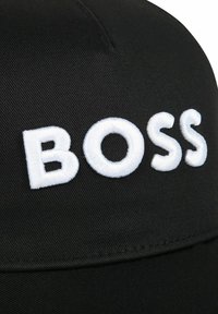 Cappello nero con una forma strutturata, caratterizzato da un logo ricamato bianco "BOSS" in rilievo sul davanti e un design in tessuto testurizzato.