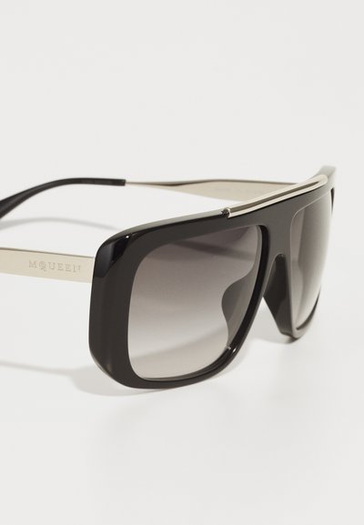 Black oversized sunglasses with a smooth frame, gradient lenses, and silver accents on the temples, featuring engraved branding on the side.
