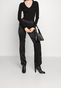 Černý přiléhavý svetr s výstřihem do V, kombinovaný s černými saténovými kalhotami se zavazováním po stranách a černými kotníkovými botami na podpatku. Černá texturovaná kabelka.