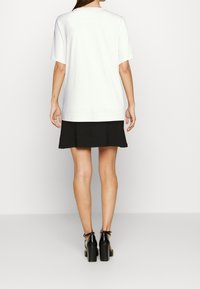 Camiseta blanca de manga corta combinada con una falda negra. La camiseta tiene un escote redondo y un corte holgado, mientras que la falda tiene un diseño simple y recto.