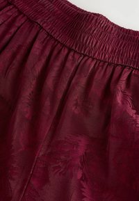 Bordeaux rok met een elastische tailleband, voorzien van een textuurlijke bloemenpatroon voor extra detail en een gladde afwerking.