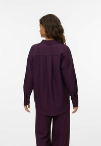 Chemise à manches longues violette avec un col, des poignets boutonnés et un tissu texturé. Le dos présente un empiècement avec des coutures subtiles.