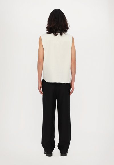 Top senza maniche di un grigio chiaro con orlo sfilacciato, abbinato a pantaloni neri larghi. Design semplice, in cotone o materiale simile.