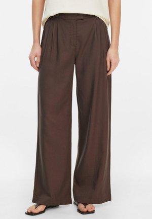 Luźne, szerokie spodnie w ciemnym brązie noszone z jasnobeżową, włożoną do środka bluzką oraz czarnymi sandałami z kwadratowym noskiem.
