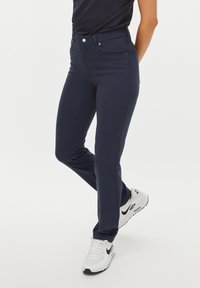 Navyblauwe, slim-fit broek van rekbare stof. Met een klassieke vijf-pocket ontwerp en een gladde textuur. Draagt met witte sneakers.