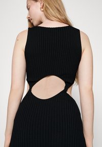 Vestido preto canelado com um design sem mangas e detalhes de costas recortadas. O material é texturizado com uma silhueta ajustada.