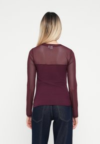 Burgundy långärmad skjorta med en genomskinlig, texturerad överdel och solid nederdel. Tillverkad av bomullsblandning med en figurnära design.
