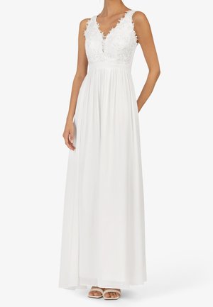 Mujer con vestido maxi blanco sin mangas con corpiño de encaje floral y falda fluida, combinado con sandalias blancas de punta abierta.