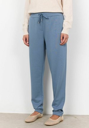 Ljusblåa sweatpants med dragsko i midjan, sidofickor och en avslappnad passform, kombinerade med beiga slip-on skor med mönstrad textur.
