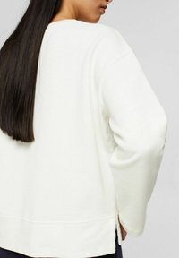 Witte sweatshirt met een relaxed fit, lange mouwen en zijsplitten. Zachte textuur en subtiele naaddetails zijn zichtbaar.