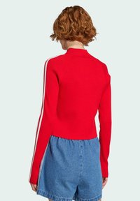 Rot gestreifter Pullover mit hohem Kragen und weißen Streifen an den Ärmeln, kombiniert mit Jeansshorts. Besitzt eine kurze Silhouette.