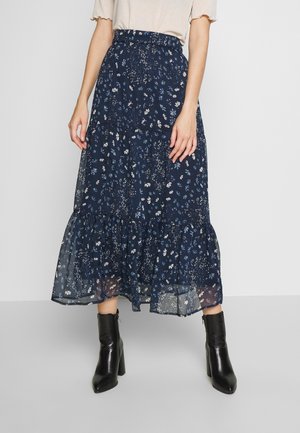 Mørkeblå maxi-nederdel i gennemsigtig stof med hvidt blomstertryk og rynket kant. Kombineret med sorte hæle ankelstøvler.