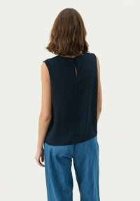 Marineblaues ärmelloses Blusenshirt mit einem Schlüssel-ausschnitt im Rücken und glattem Stoff. Kombiniert mit hellblauen weit geschnittenen Jeanshosen.
