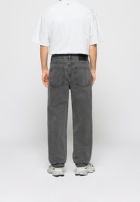 Jean gris coupe décontractée avec jambe droite, design à cinq poches et empiècement arrière. Assorti à un t-shirt gris ample et des baskets claires.