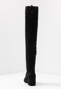Botas de ante negras por encima de la rodilla con tacón grueso, detalle de cordón en la parte superior, textura suave y una silueta elegante.