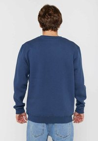 Navy blue sweatshirt featuring a crew neck, long sleeves, and ribbed cuffs and hem. Made of soft, textured fabric. Back view shown.
