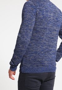 Dunkelblauer Strickpullover mit helleren Sprenkeln, Rundhals und gerippten Bündchen. Die Textur ist weich und gemütlich mit einer figurbetonten Passform.