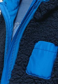 Fleecejacke in Dunkelblau mit einer weichen, strukturierten Oberfläche; verfügt über eine glatte, blaue Reißverschlusstasche und ein gemütliches Innenfutter.