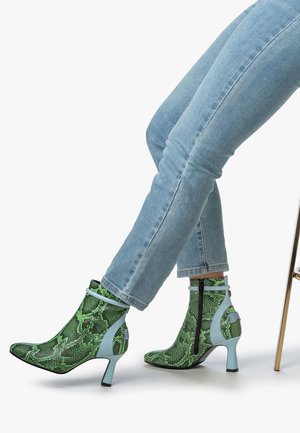 Stivali alla caviglia a stampa serpentosa verde con punta affilata e tacchi azzurri. Presentano una chiusura con zip e dettagli a contrasto sul tacco.