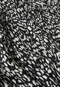 Tissu noir avec un motif abstrait blanc, présentant une texture douce et de légères plis pour le mouvement et la drapé.