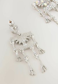 Pendiente de plata colgante con diseño abstracto texturizado y múltiples segmentos enlazados que terminan en puntas redondeadas sobre un fondo claro.