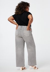Jeans gris à jambe large avec une taille haute, dotés de poches arrière et d'une texture décolorée. Associés à un t-shirt noir et des sandales à talons de couleur claire.