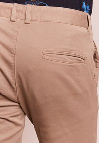 Khaki kalhoty s hladkou texturou, rovný střih a zadní kapsa s zakřiveným otvorem. Pásky na opasek v pase.