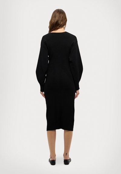 Rochie neagră tricotată cu mâneci lungi, textură rigletă și siluetă ajustată. Lungime până la jumătatea gambei cu o ușoară curbă la talie. Design simplu.